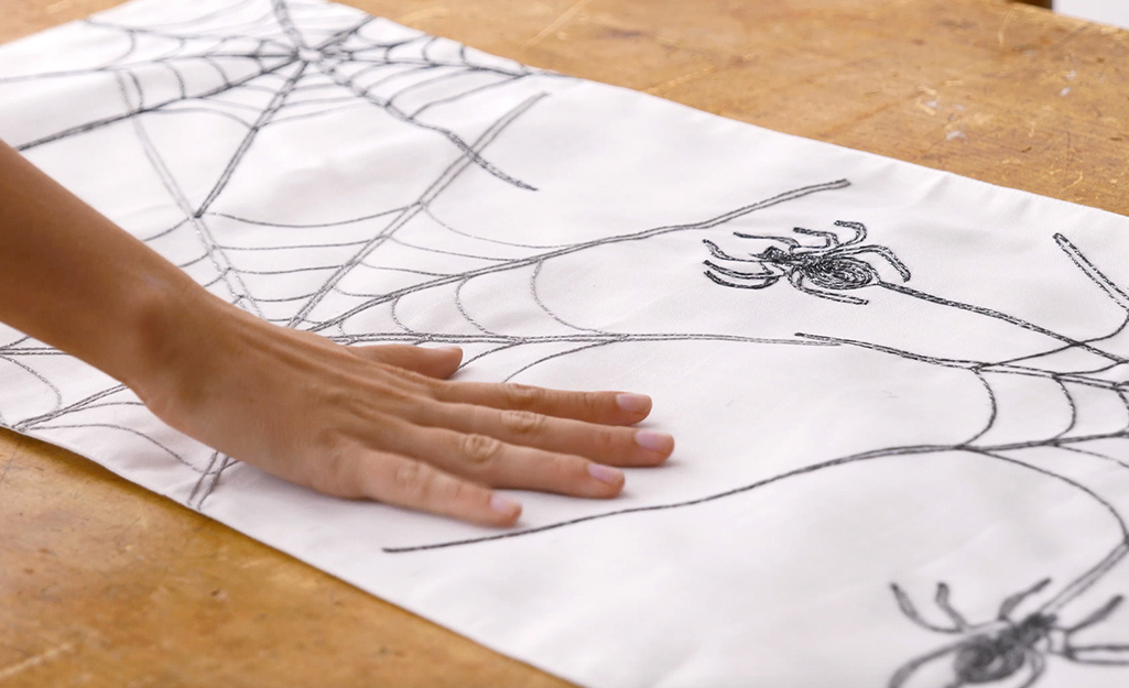 A hand smooths out a Halloween themed table runner. A hand smooths out a Halloween themed table runner.
