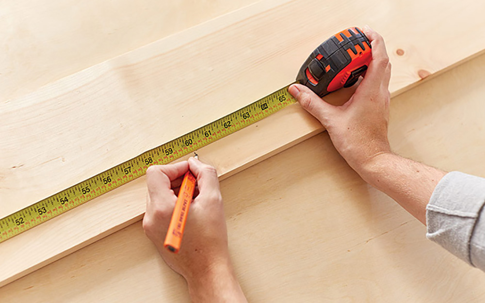A person measuring and marking a wood board.