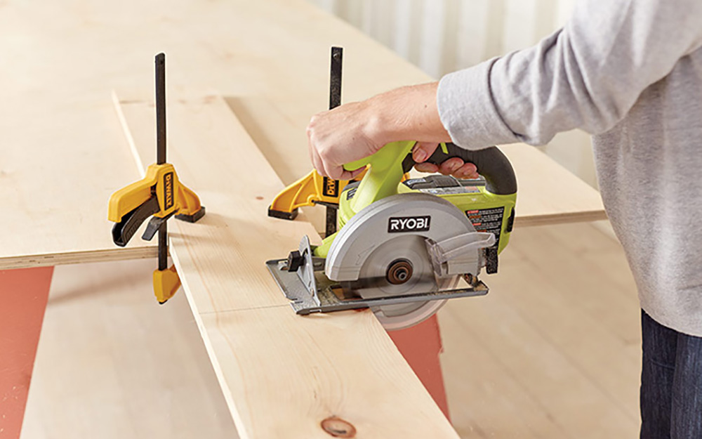 A person cutting a wood board with a circular saw.