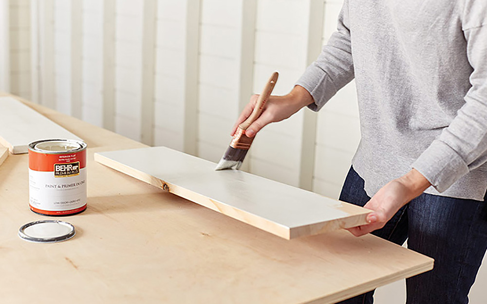 A person painting a wood board with white paint.