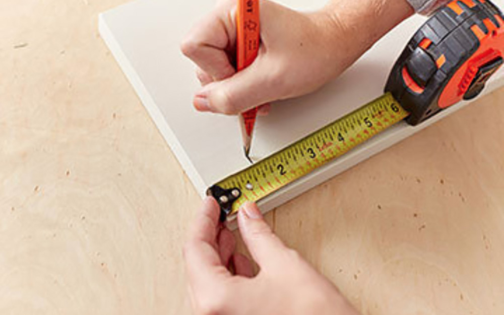 A person measuring and marking a painted wood board.