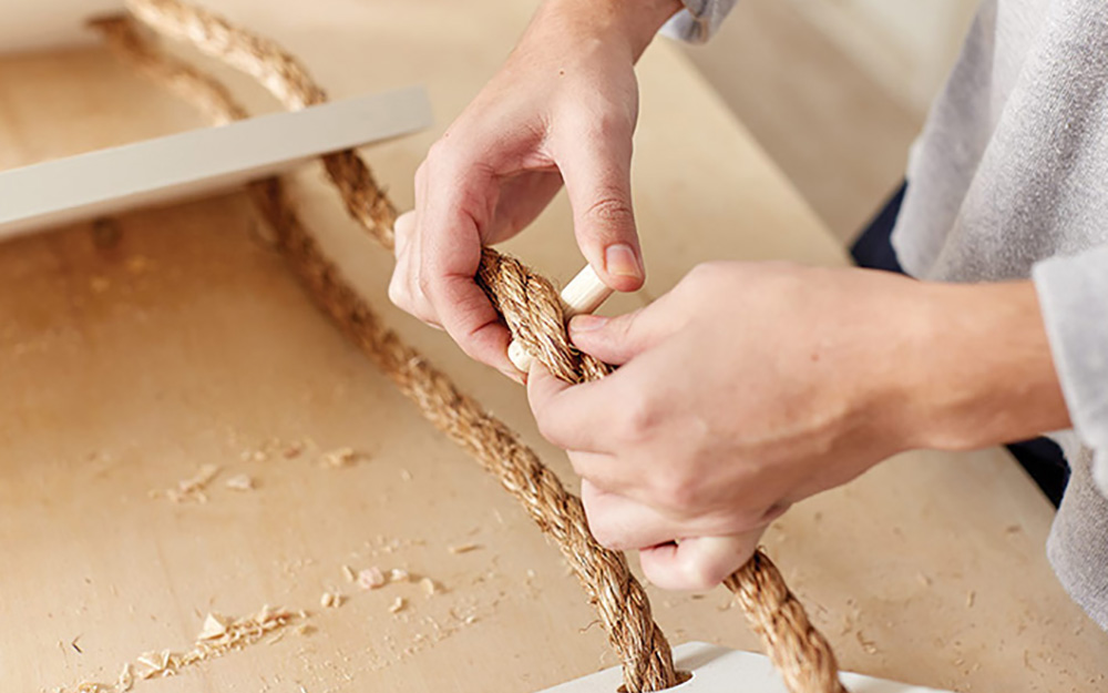 A person inserting a wooden dowel into the rope under the shelves.