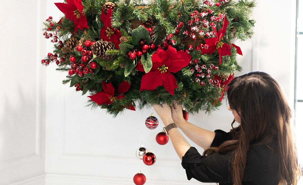 A woman hangs ornaments from a planter.