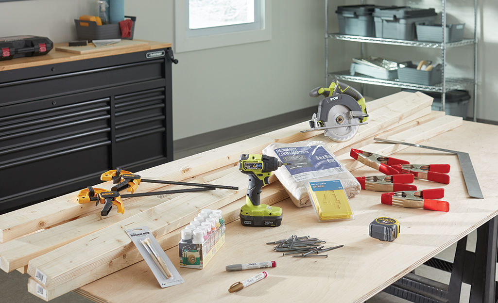 Lumber, a drill, a circular saw, clamps and other tools and materials lay on a work bench.