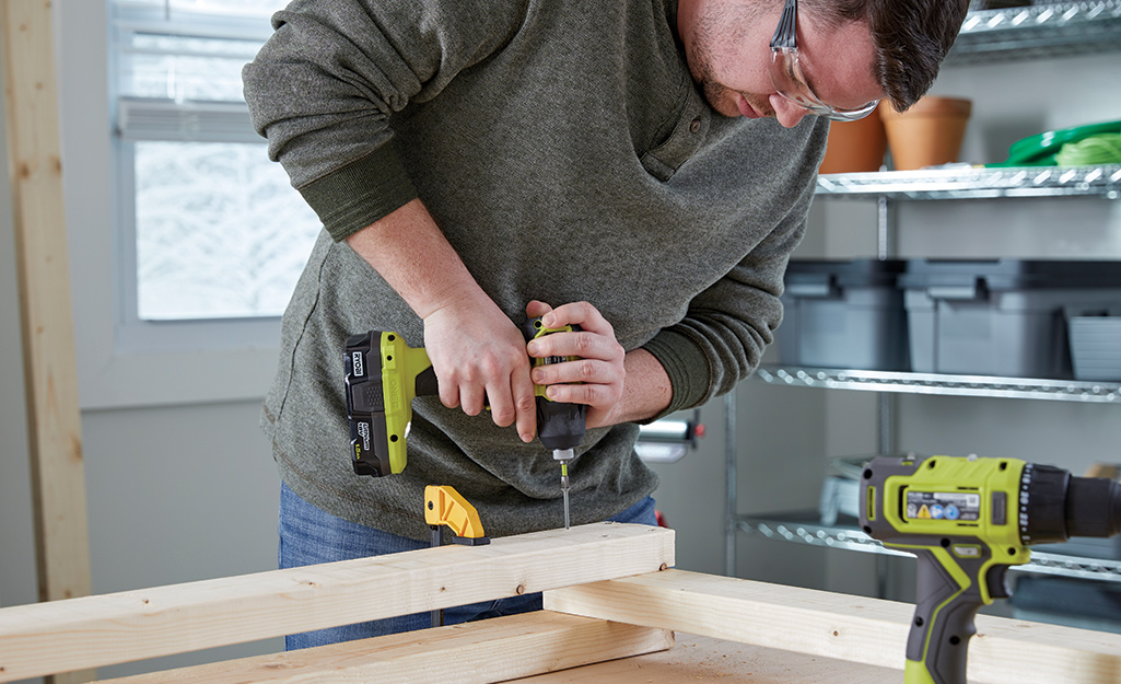 A man in a workshop screws a wood stand together.