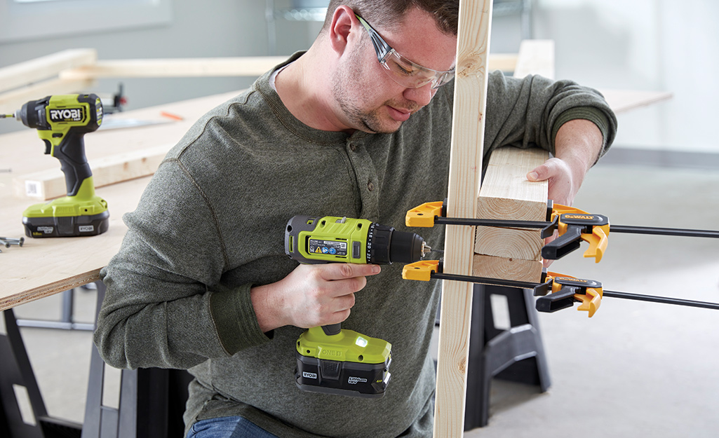 A man in a workshop attaches wooden feet to the frame of a photo booth.