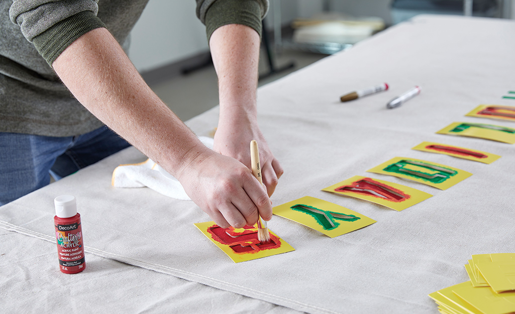 A person uses a brush, paint and stencils to add letters to a piece of canvas.