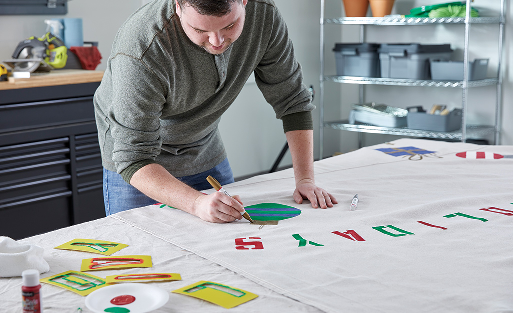 A man uses a paint pen to add a detail to a ornament painted on a canvas backdrop.