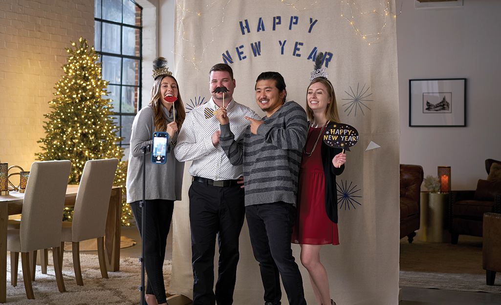 Four people with props get their photo taken in front of the backdrop of a DIY holiday photo booth.