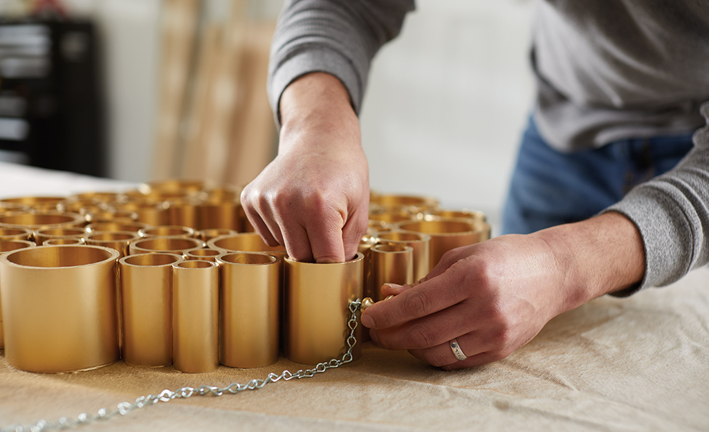 Someone attaching a hanging chain to a gold PVC pipe holiday wreath.