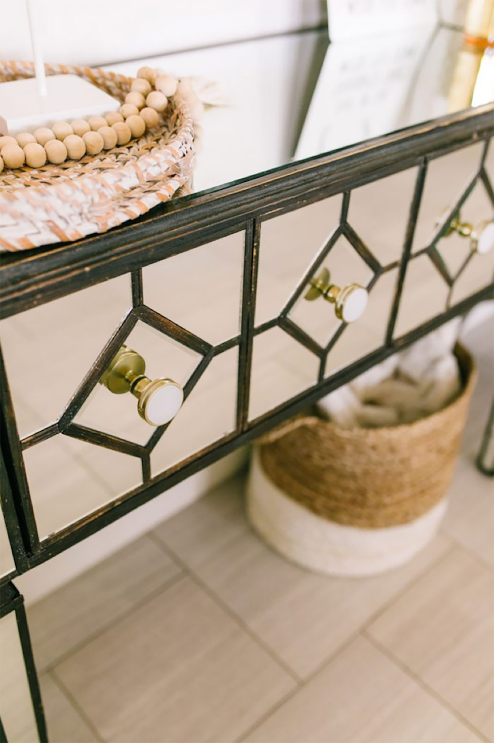 A natural jute decorative storage basket sitting under a mirrored console table.