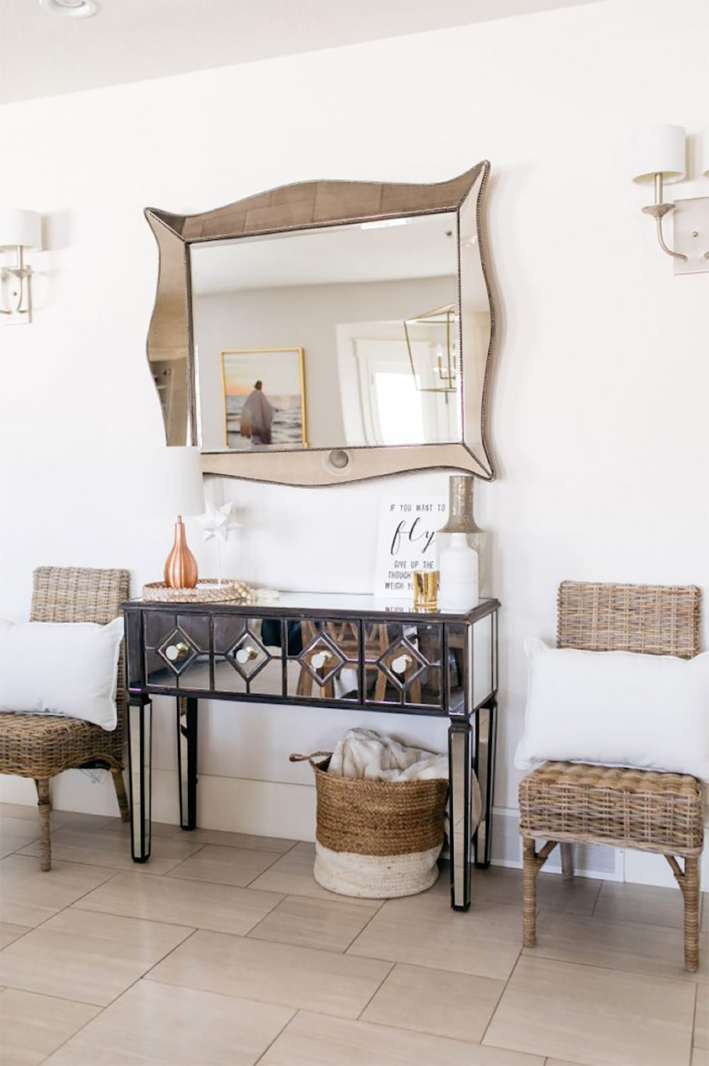 A black and mirrored console table with natural rattan chairs on either side.