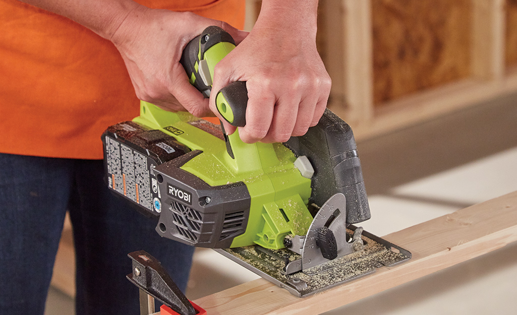 A person uses a power saw to cut a board.