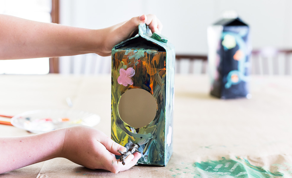 A person adding a twig perch to a milk carton bird house.