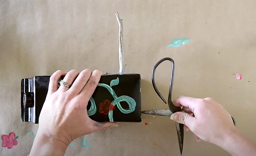 Someone using scissors to punch a hole in bottom of the bird house.