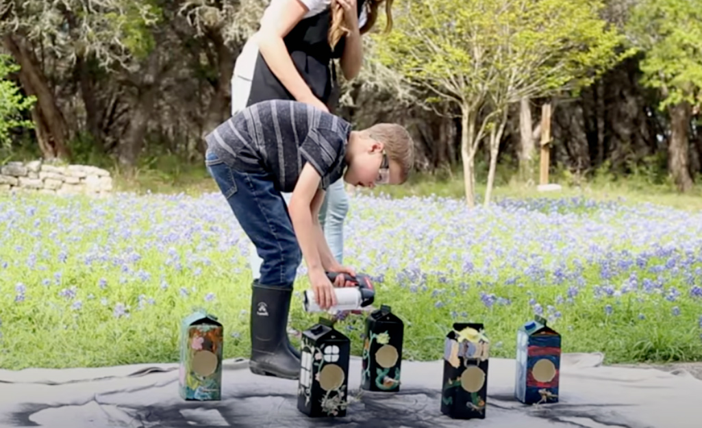 A boy spraying sealant on a DIY bird house.