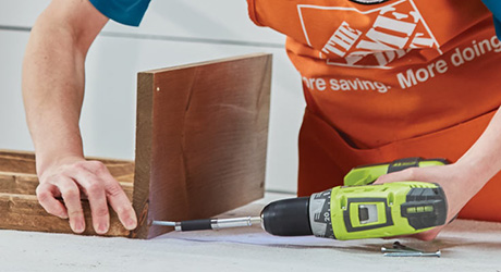 A person using a drill driver to attach two boards together. A person using a drill driver to attach two boards together.