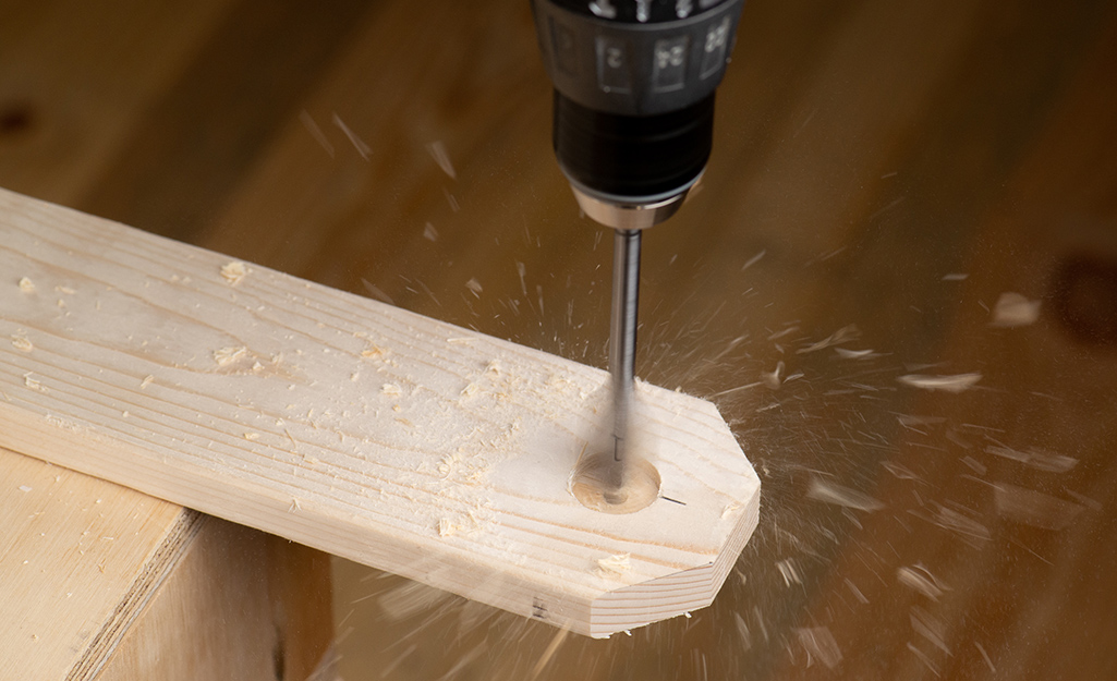 A person drills the holes into wood with a drill bit.