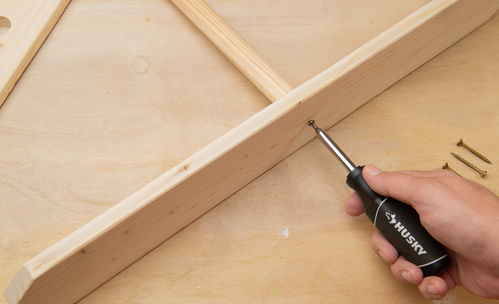 A person uses a screwdriver to attach a dowel to part of the wood frame.