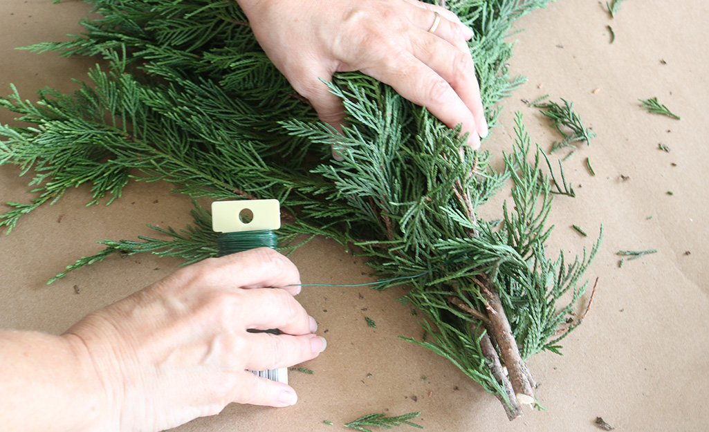 A person bundling pine branches together with floral wire. A person bundling pine branches together with floral wire.