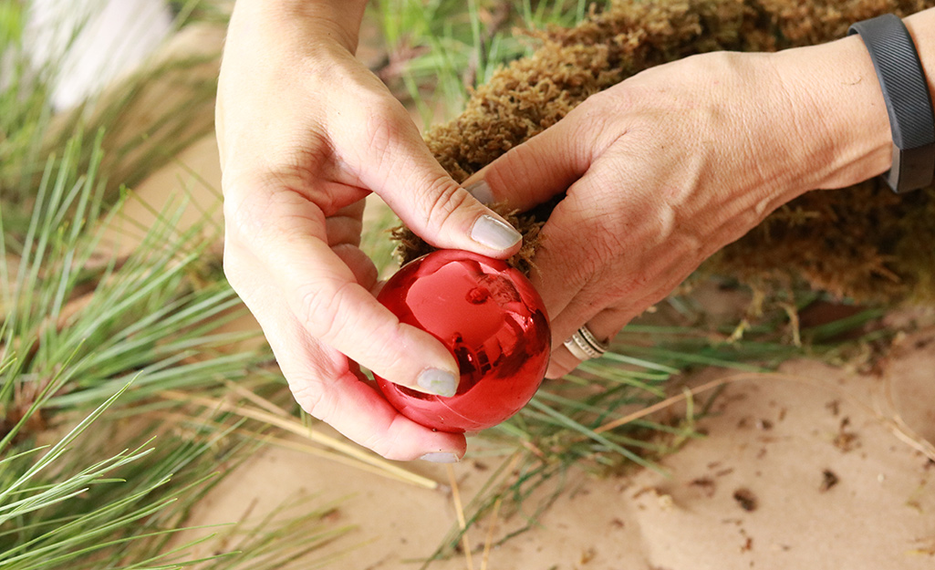 A person attaching a red ornament to the end of the moss hat. A person attaching a red ornament to the end of the moss hat.