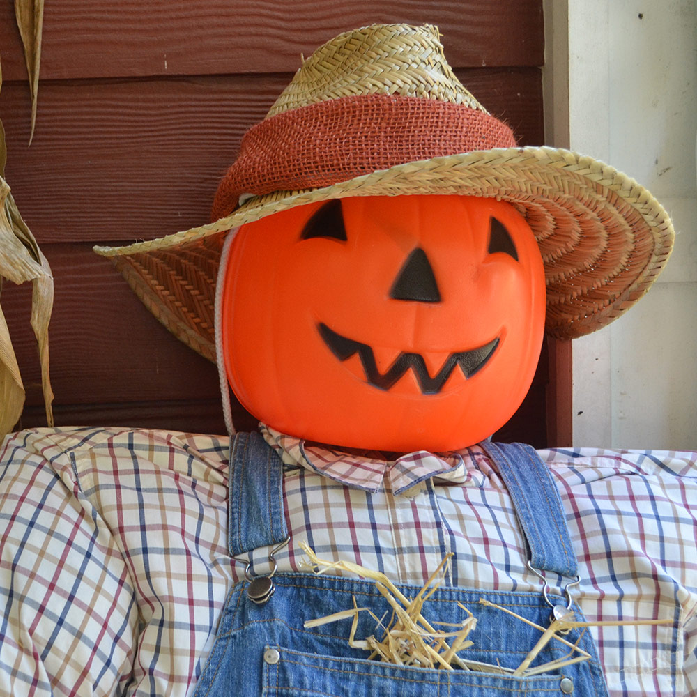 A homemade scarecrow sits on a front porch.