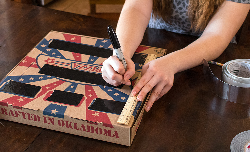 A person drawing lines on a pizza box.