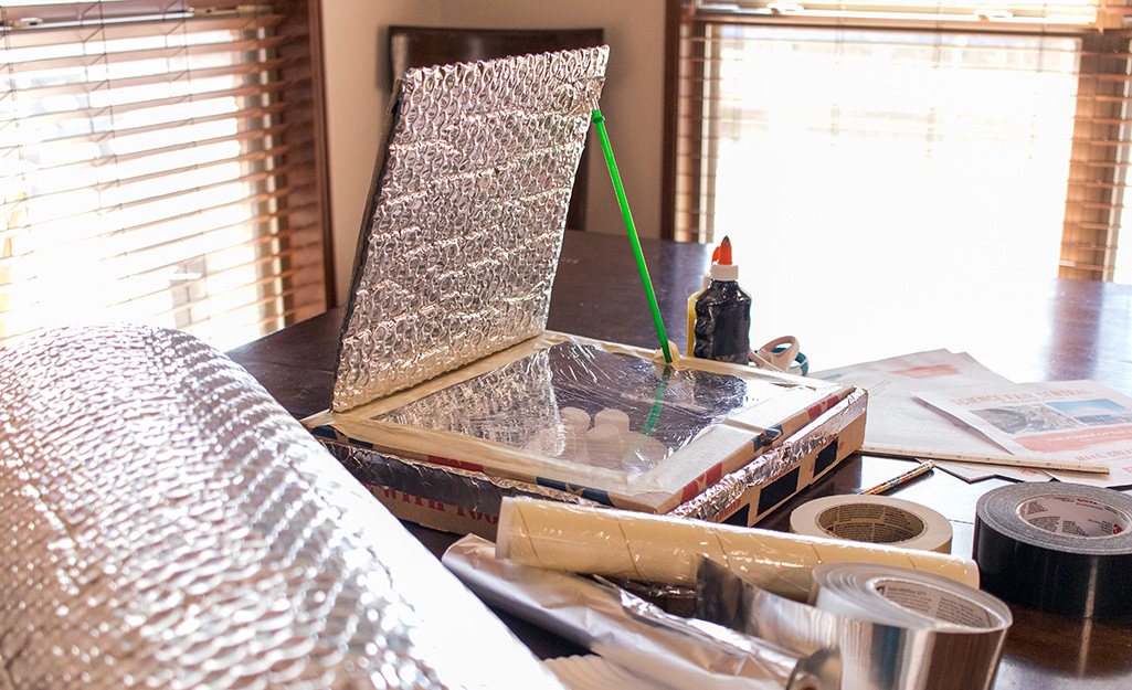 A homemade solar oven surrounded tape, glue and other craft supplies.