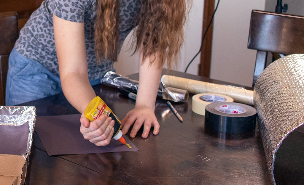 A girl applying glue to cardboard paper.