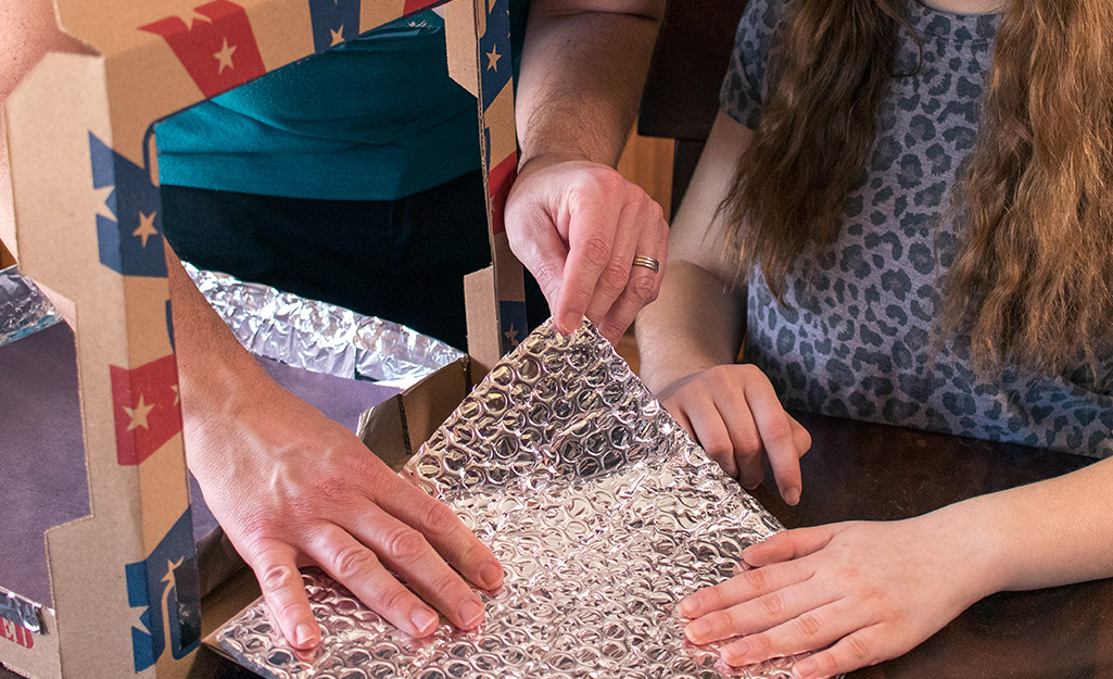 Two people adjusting foil in a pizza box.