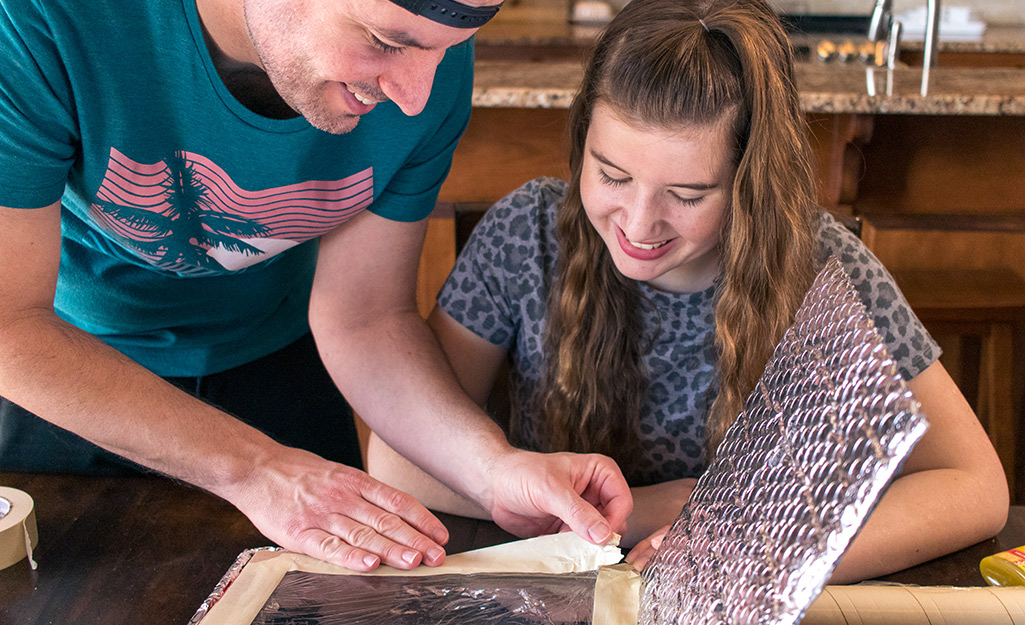 Two people adding tape to the inside of a pizza box.