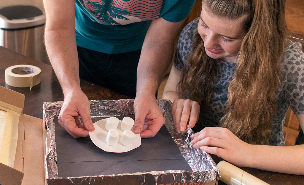 A man setting marshmallows into a foiled pizza box.