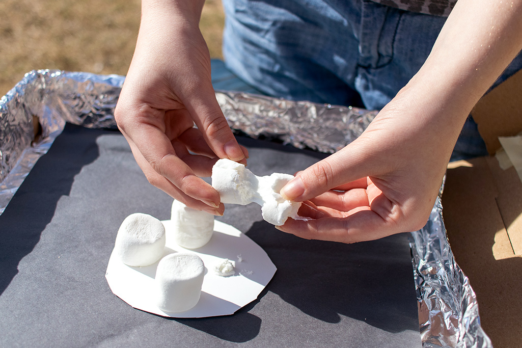 A person pulling apart marshmallows in a homemade solar oven.