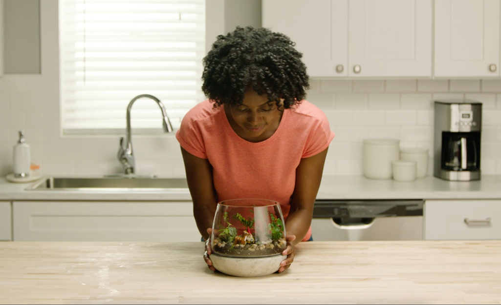 A woman standing over a terrarium. 