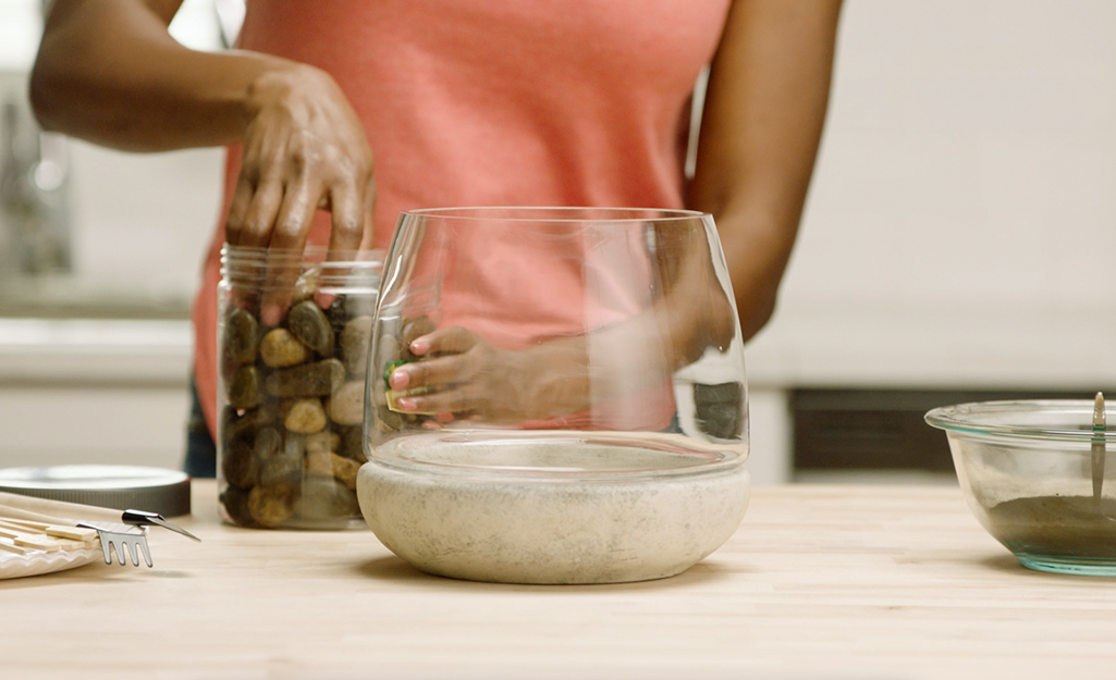 A woman adds rocks to a terrarium 