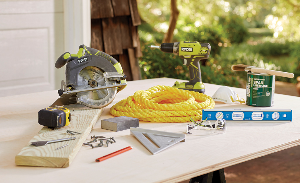 A circular saw lays on a board by rope, a drill, a can of stain, a sanding block, a level and other items needed to make a tree swing.