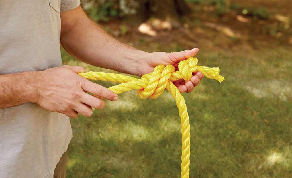 A person ties a knot in a piece of yellow rope.