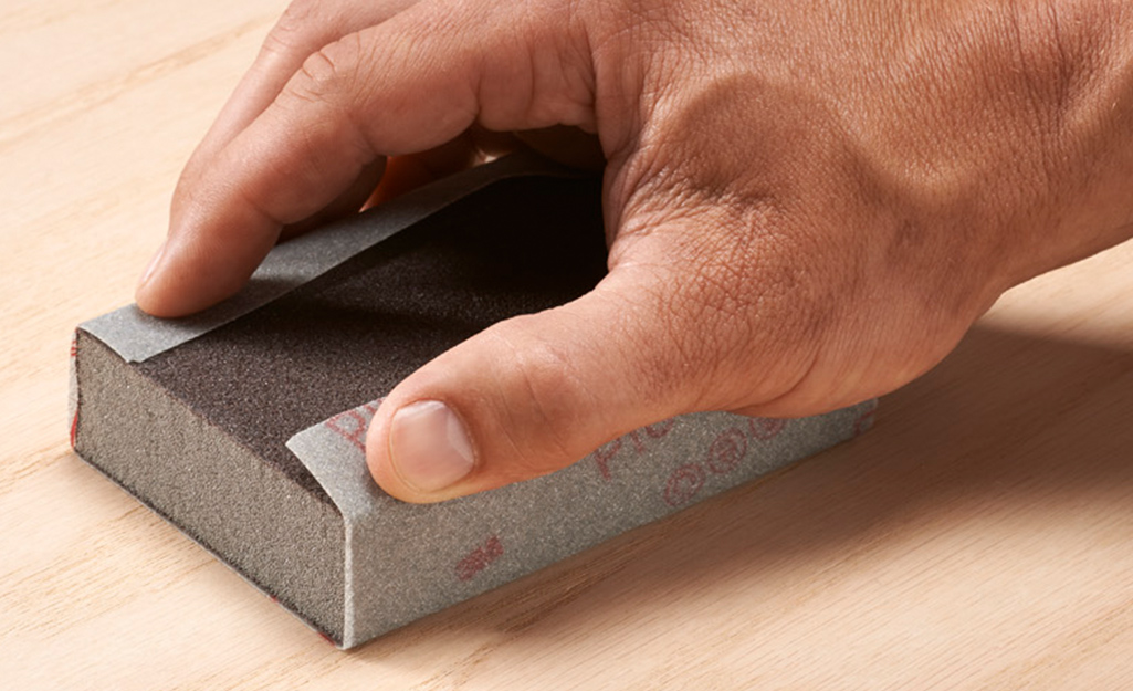Someone using a sanding block and sandpaper to smooth a board for a tree swing. Someone using a sanding block and sandpaper to smooth a board for a tree swing.