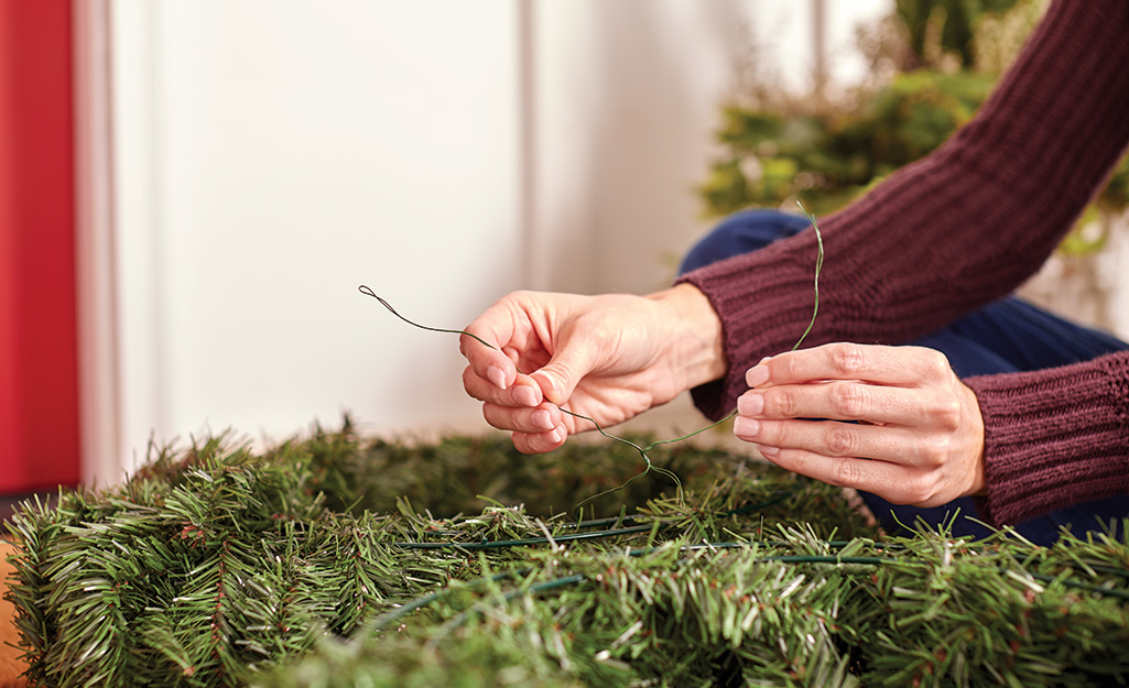 A woman twists together floral wire while connecting two holiday wreaths.