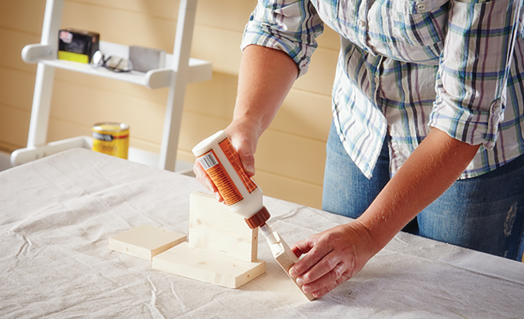 A person adds wood glue to the edges of wood.