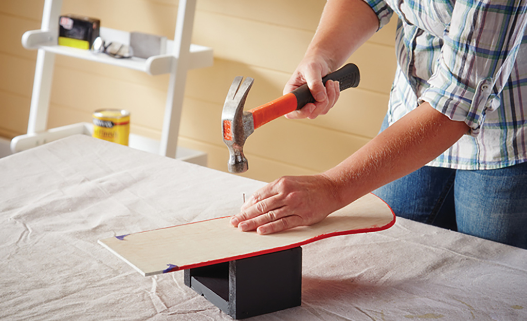 A person nails a wood stocking to the front of a box.