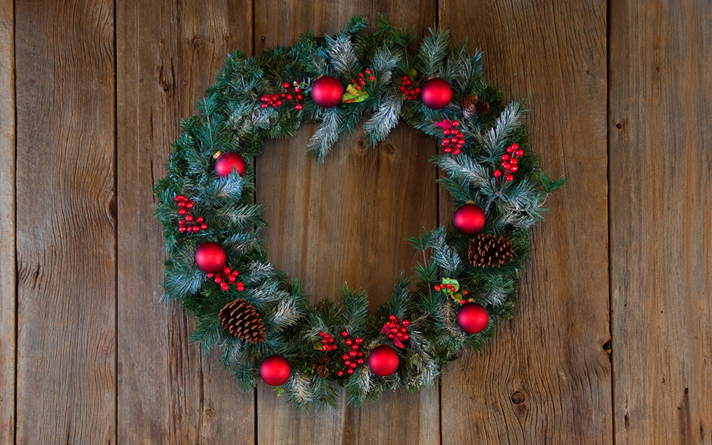 A Christmas wreath decorated with greenery and red ornaments hanging on a door.