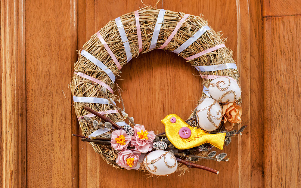 Straw wreath with ribbons, faux flowers and a wooden bird.