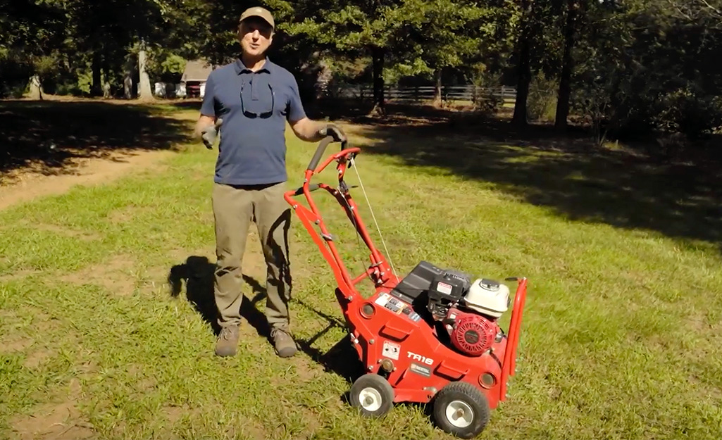 A person rolls a spike aerator over a lawn.