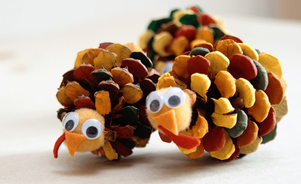Two colorful turkey pinecones sit on a table.