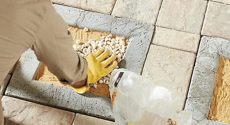Someone wearing work gloves to press pebbles over a layer of sand in a pathway paver.