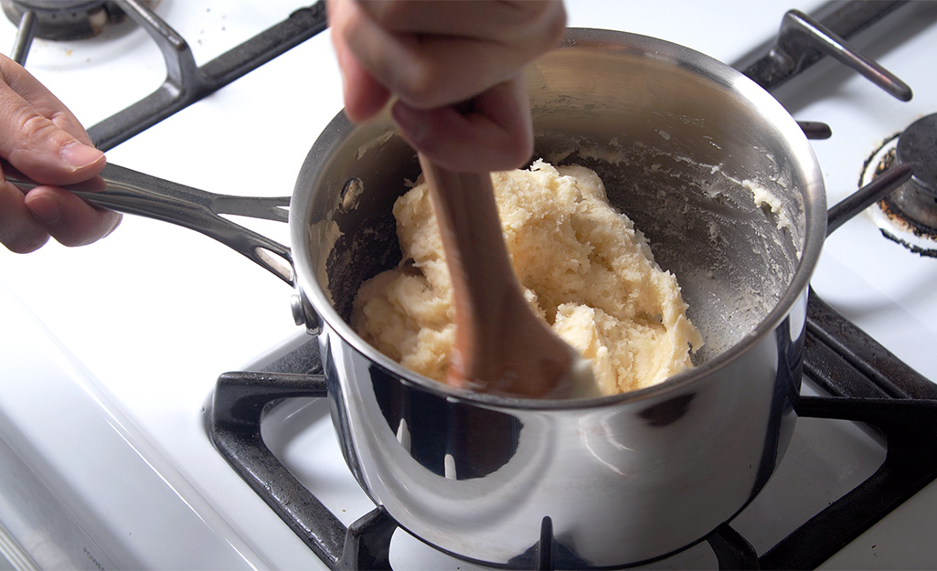 A person mixes flour, water and other ingredients in a sauce pan.