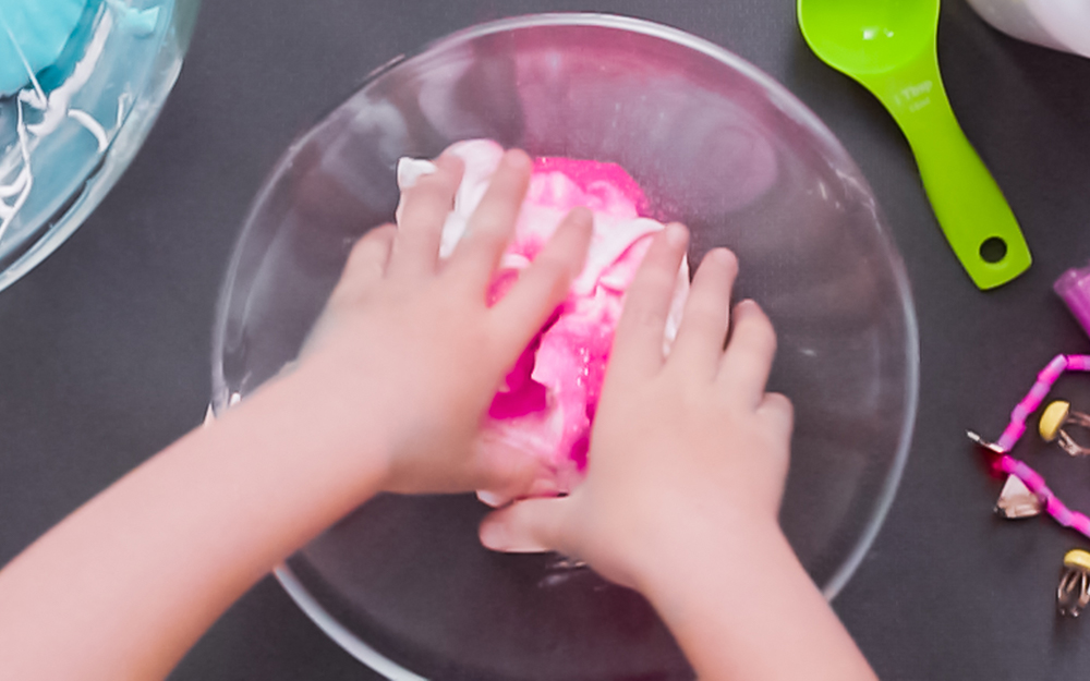 A hand mixing pink slime in a bowl