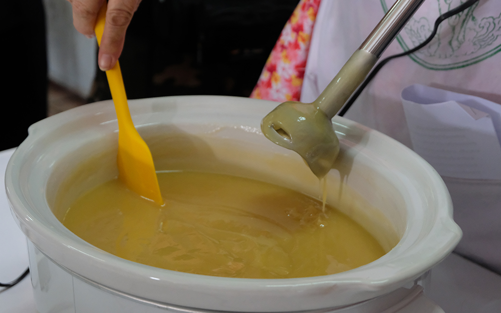 A person mixing soap in a slow cooker with a spatula and immersion blender. A person mixing soap in a slow cooker with a spatula and immersion blender.