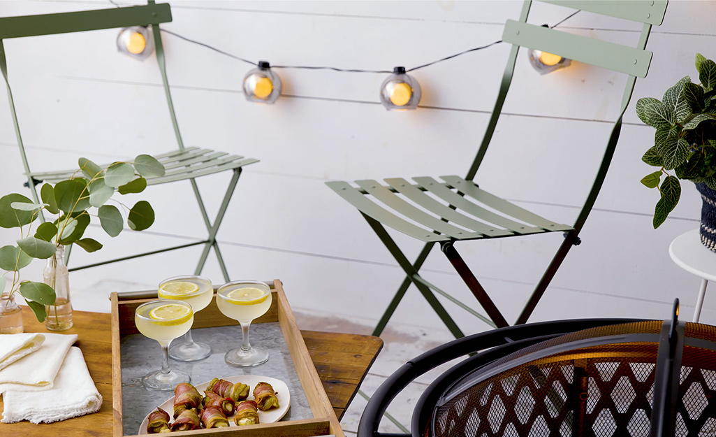 An outdoor space with string lights, a fire pit, seating, food and drink. An outdoor space with string lights, a fire pit, seating, food and drink.